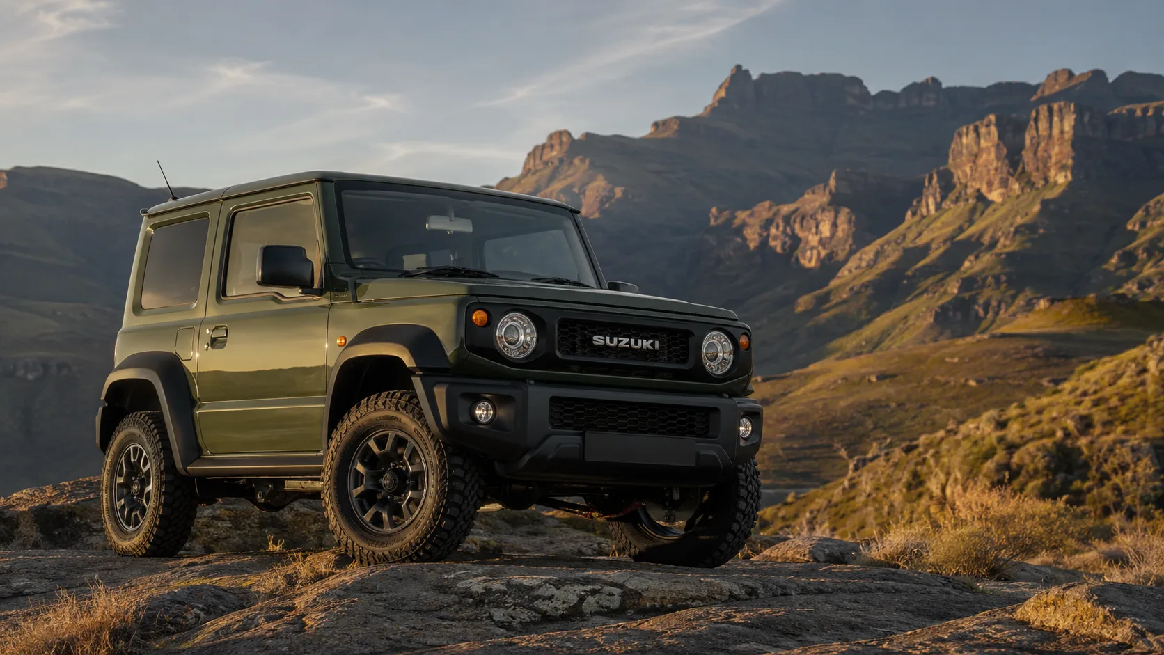 Green Suzuki Jimny JB74 parked on a rocky mountain outcrop at sunset