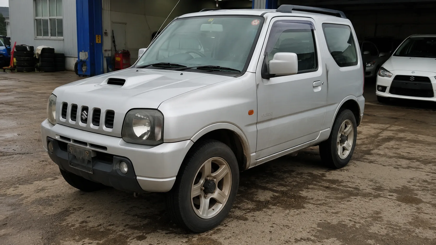 Third-generation silver Suzuki Jimny JB23 parked on a workshop forecourt